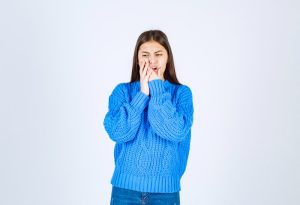 portrait of teenager girl in blue sweater having toothache on white